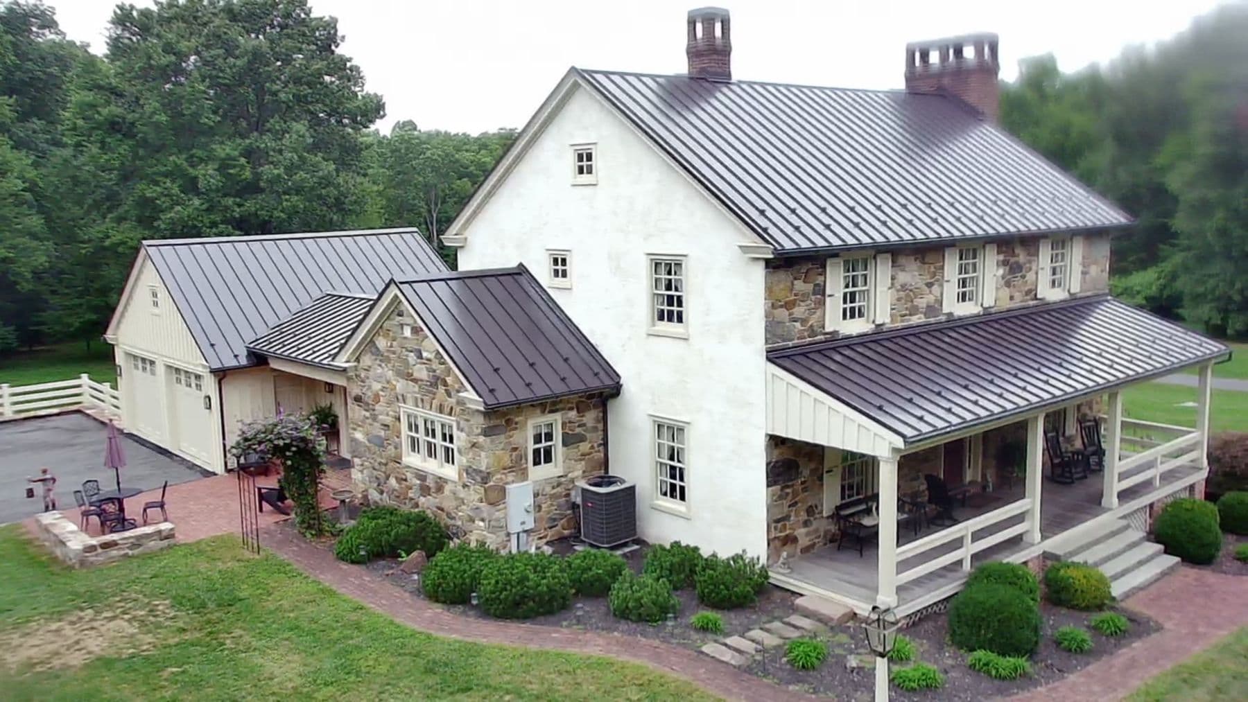 Standing-seam metal roof on a stone farmhouse with a wraparound porch, installed by King's Roofing & Siding